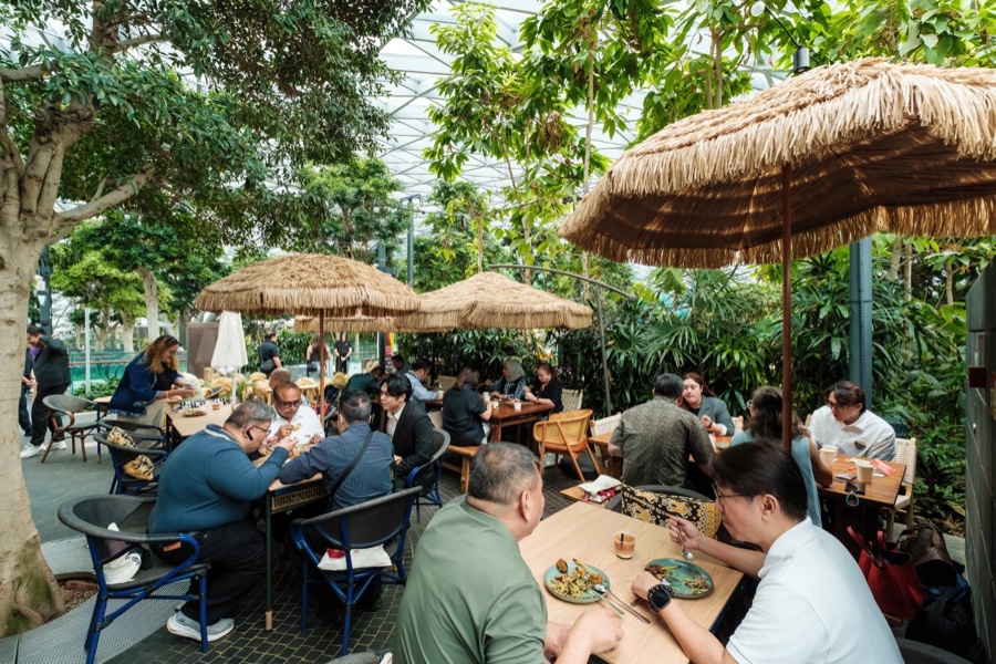 Diners at tables under thatched umbrellas inside Jewel Changi Airport
