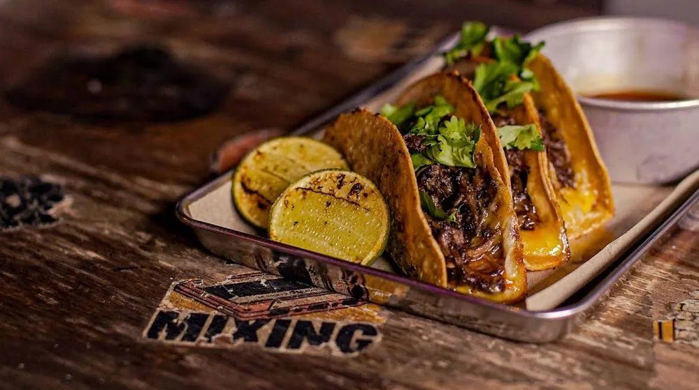 Three beef birria tacos with cilantro, grilled lime and a cup of consommé