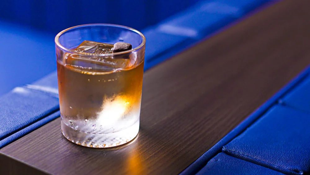 A Milo Old Fashioned on ice on a dark bar table at Brooklyn Bar