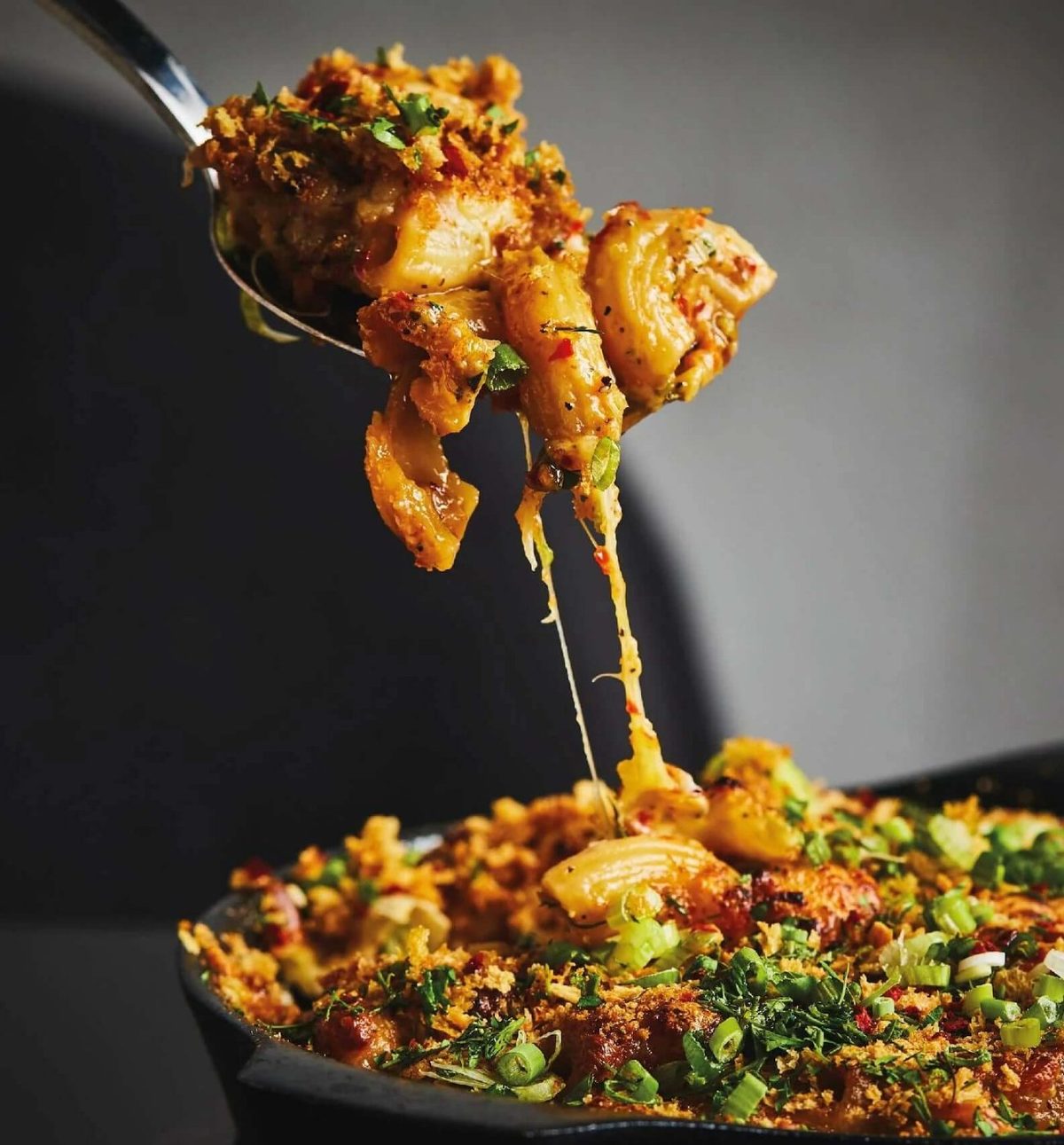 A spoonful of spicy mac and cheese being lifted from a skillet at Cheeselads