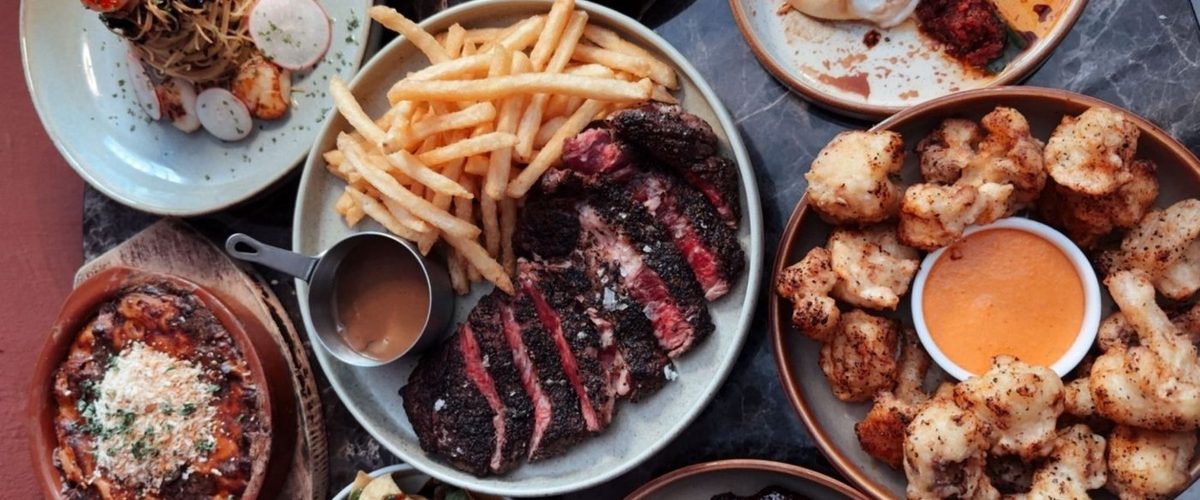 A table spread of steak, fries, fried cauliflower and pasta at Cheeselads