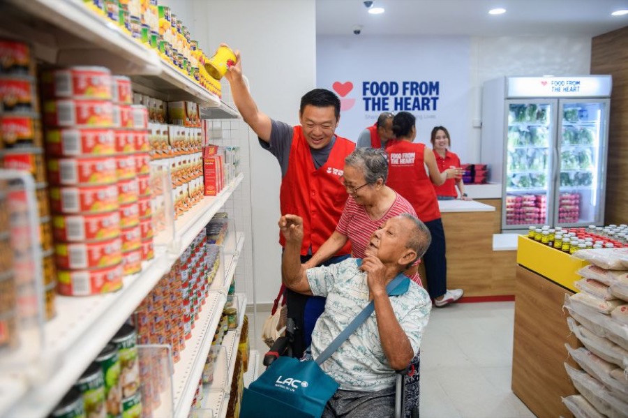 A Food From The Heart volunteer helps beneficiaries pick canned food off the shelves inside the Community Shop