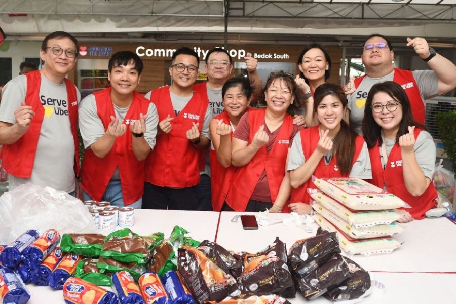 Volunteers in red vests outside the Community Shop @ Bedok South storefront with donated food on the table