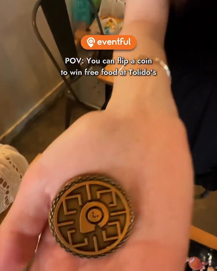 The bronze Eventful Coin resting in a diner's palm at Tolido's Espresso Nook, pin side up