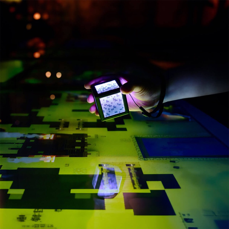 A visitor using the handheld Prismarine device over a projected Minecraft map inside Minecraft Experience: Villager Rescue