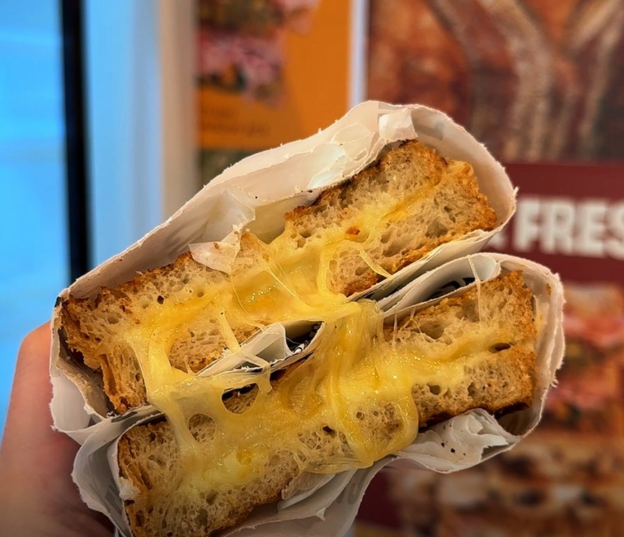 Half a classic grilled cheese sandwich in wax paper, cheese pulling apart, held up at the PRESSED! kiosk