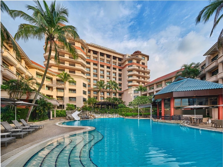 The outdoor pool with water slide at Paradox Singapore Merchant Court, framed by palm trees and the hotel tower