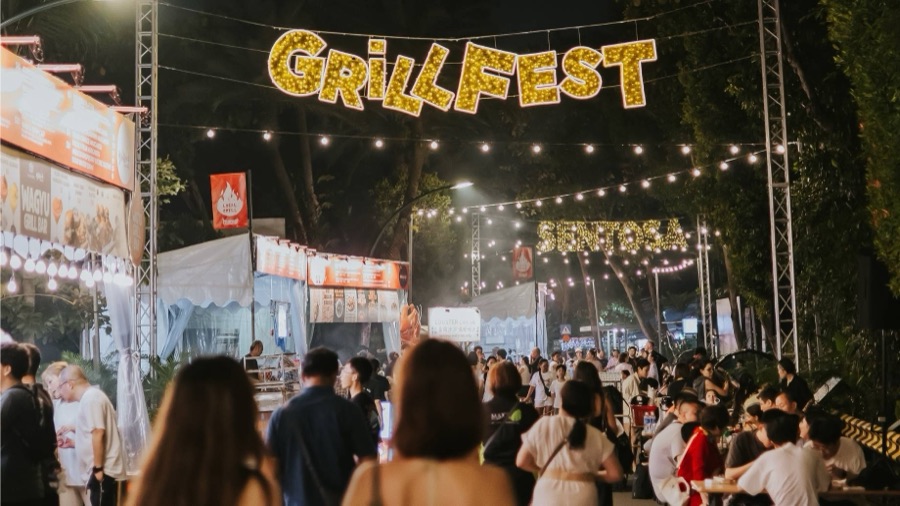 The lit-up GrillFest entrance sign over a crowded festival stretch at Sentosa in the evening