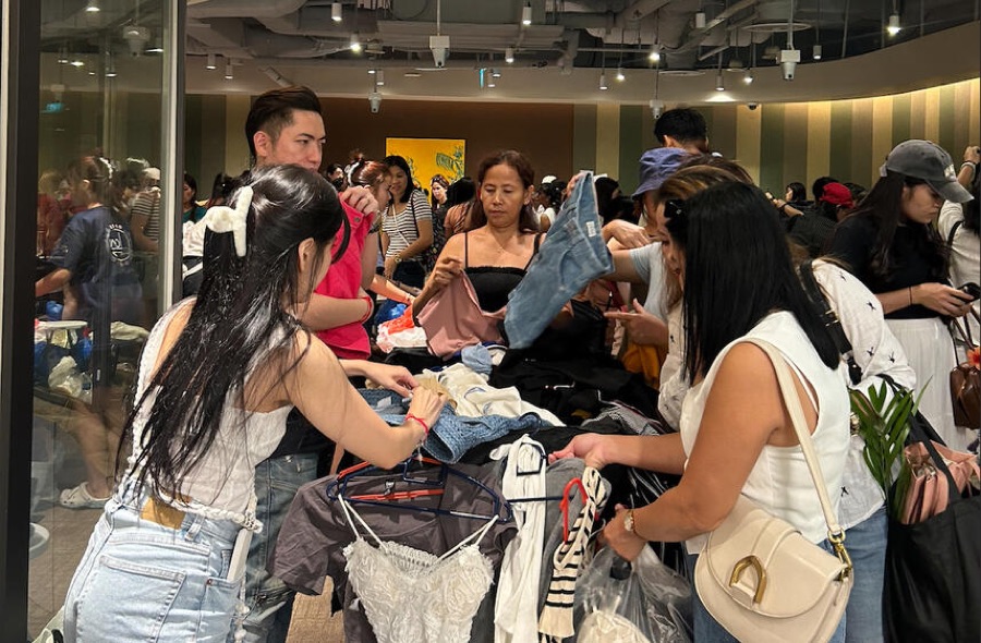 Shoppers digging through racks and tables of secondhand clothes at a Fleawhere flea market