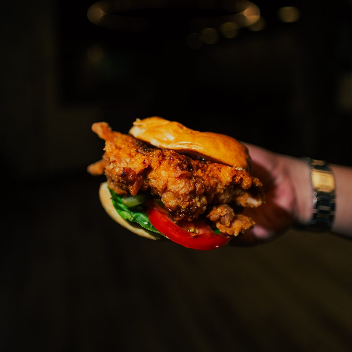 A hand holding a crispy fried chicken burger at Sonic Bistro