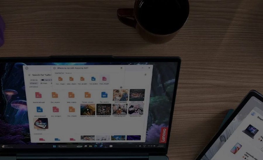 A Lenovo Yoga laptop open on a wooden desk next to a tablet and a mug of coffee