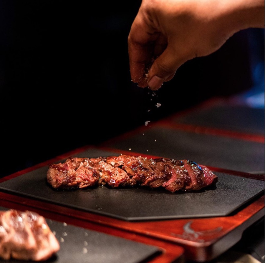 Chef seasoning a sliced feather blade steak on a slate at The Feather Blade, Tanjong Pagar
