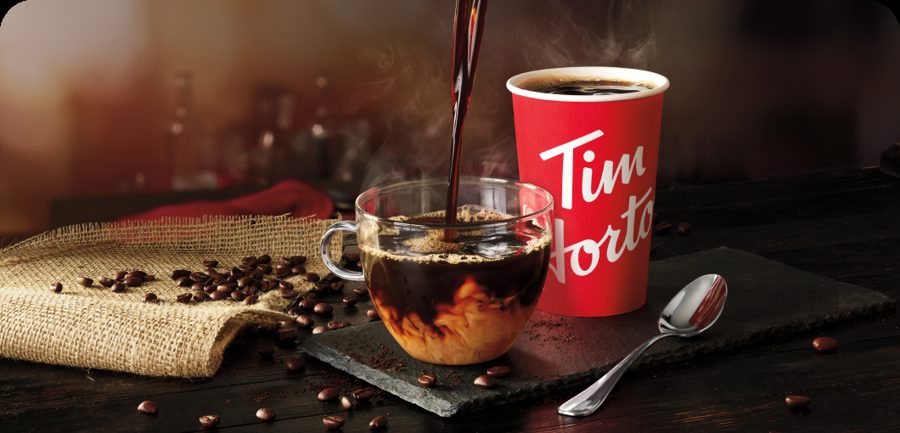 Coffee being poured into a glass beside a red Tim Hortons cup