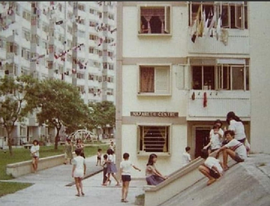 Children playing outside an old HDB block in Singapore, with laundry poles and a dome climbing frame in the background